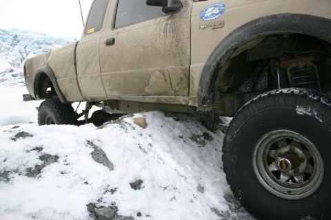2003 Jeep TJ - A tan pickup truck navigates a snowy, rocky path near a glacier.
