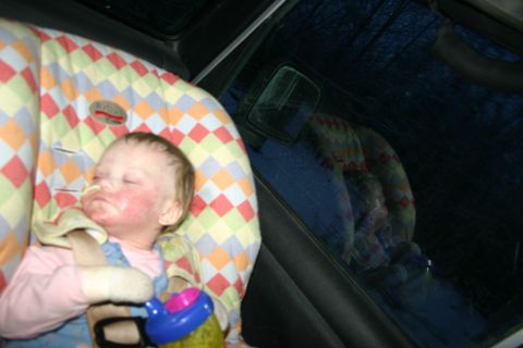 2003 Jeep TJ - A baby sleeps soundly in a colorful car seat, with the dark, wooded exterior reflected in the car window.