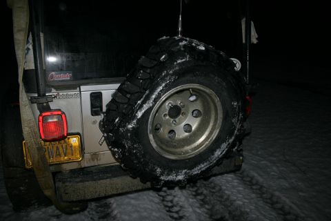 2003 Jeep TJ - Rear view of a silver Jeep Wrangler with a spare tire mounted, parked in a snowy area at night.
