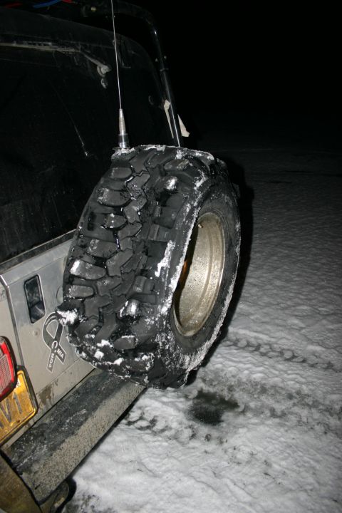 2003 Jeep TJ - A spare tire is mounted on the rear of a 2003 Jeep TJ, covered in snow, with an antenna visible.