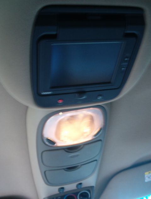 2000 Ford Excursion - The overhead console of a vehicle features a flip-down screen and a bright interior light, with storage compartments below.
