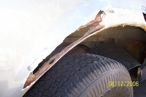 close-up of heavily rusted metal in a vehicle's wheel well, showing a tire and part of the undercarriage