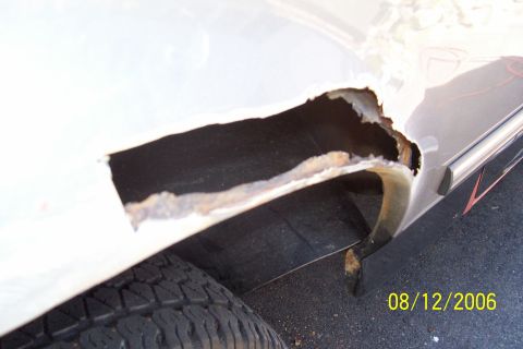 1995 Ford Bronco - The rear wheel well of a white vehicle shows significant rust and decay, revealing the inner structure.