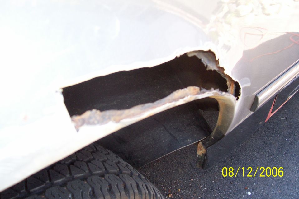 White vehicle's rear wheel well with extensive rust damage and a hole exposing the interior