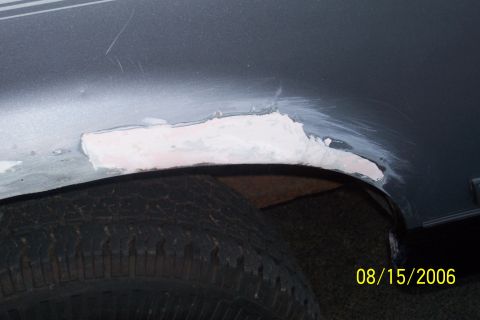 1995 Ford Bronco - Body filler is applied to a damaged area near the wheel well of a vehicle.