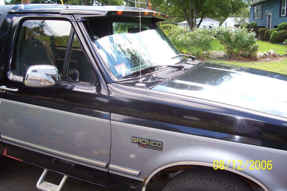 Side view of a black and silver 1995 Ford Bronco. Has a chrome side mirror and step bars