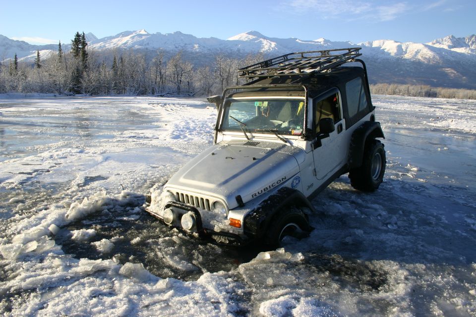 Silver 2003 Jeep TJ Wrangler with roof rack stuck in icy water, mountains in background