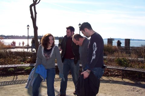 2001 Ford Crown Victoria - Four individuals converse in a park setting, with a body of water and distant structures visible behind them.