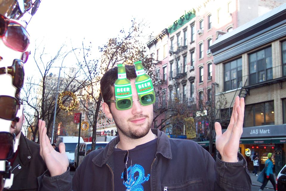 guy with beer bottle glasses on a city street, buildings and trees in background