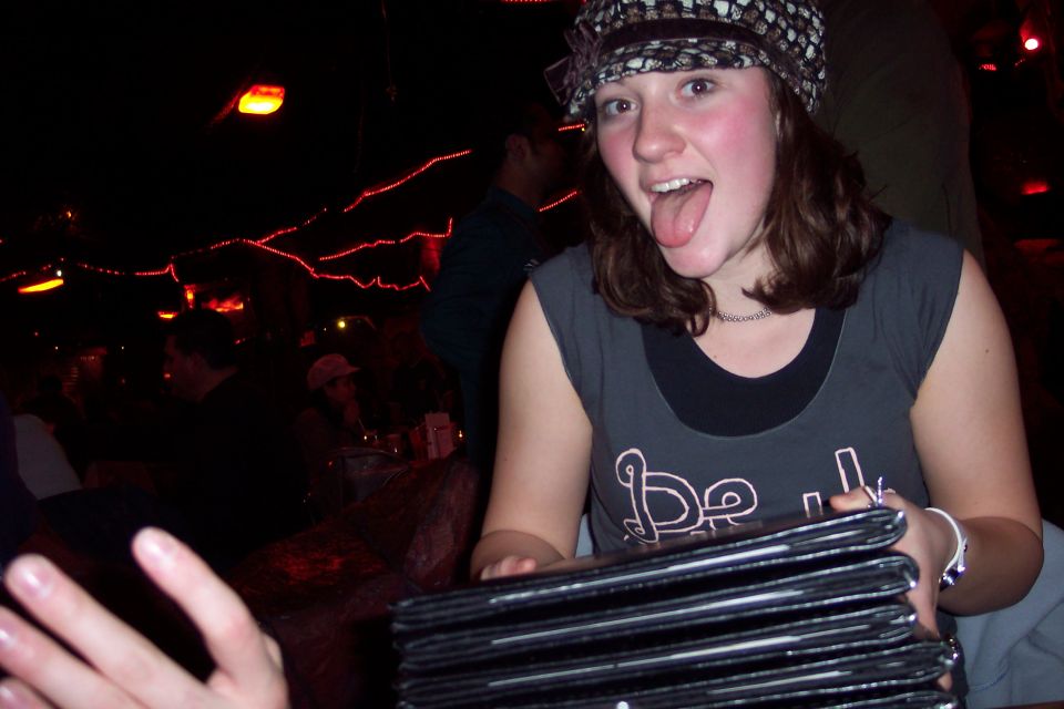 Woman in a hat sticking her tongue out while holding a stack of menus