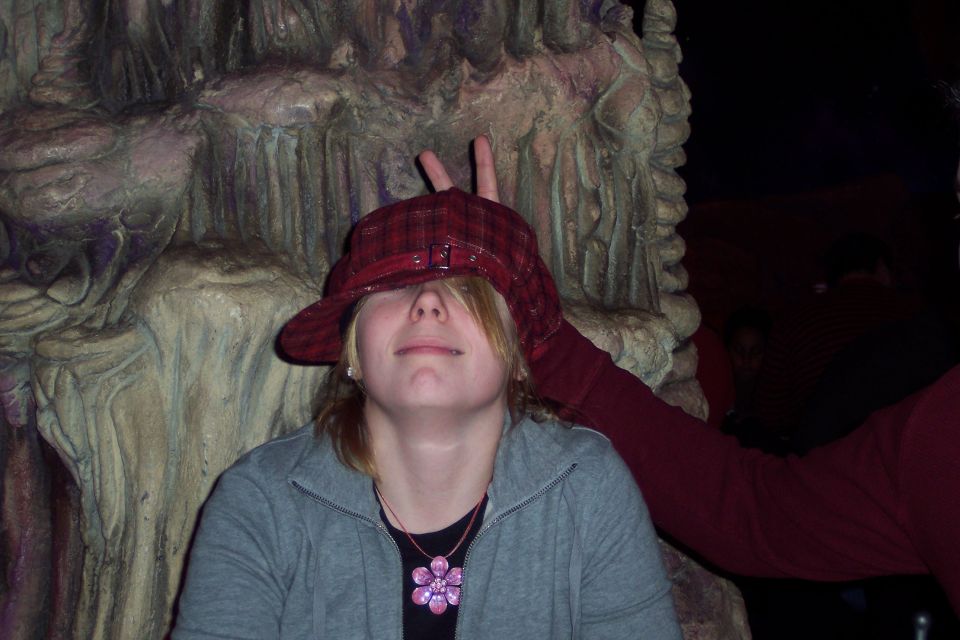 Person with a hat covering eyes, bunny ears gesture behind head