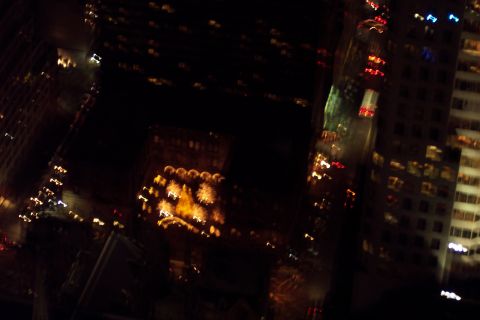 2001 Ford Crown Victoria - Blurry nighttime aerial view looking down on a dense city block from a high vantage point, with lit office windows, an illuminated building…