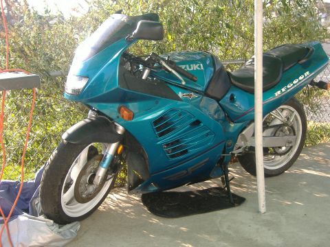 2001 BMW 3 Series - A teal Suzuki motorcycle is parked on a concrete surface next to a white pole and some bushes.
