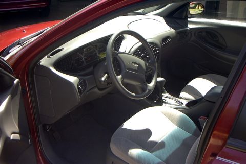 1999 Ford Taurus - The interior of a red car, showing the dashboard, steering wheel, and seats, with "SUPERMOTORS" branding visible.