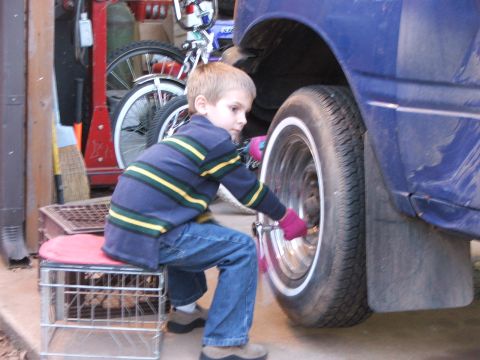 1990 Dodge Shadow - Young boy attempts to work on a car wheel in a garage setting.