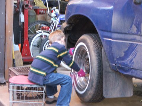 1990 Dodge Shadow - A young boy in a garage attempts to work on the wheel of a blue vehicle.