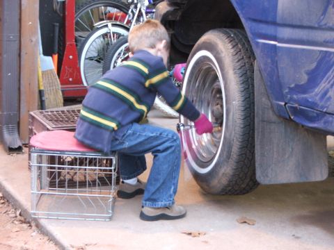 1990 Dodge Shadow - A child attempts to work on a car wheel, with bicycles visible in the background.
