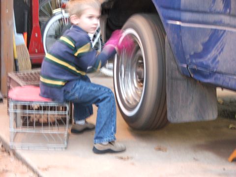 1990 Dodge Shadow - A young boy sits on a crate and cleans the wheel of a vehicle, which has a whitewall tire.