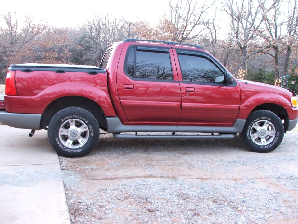 Red 2003 Ford Sport Trac pickup truck parked on gravel and concrete