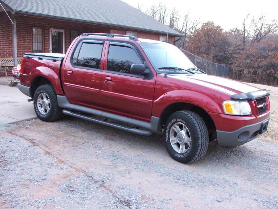 Red 2003 Ford Sport Trac parked on gravel in front of a brick house
