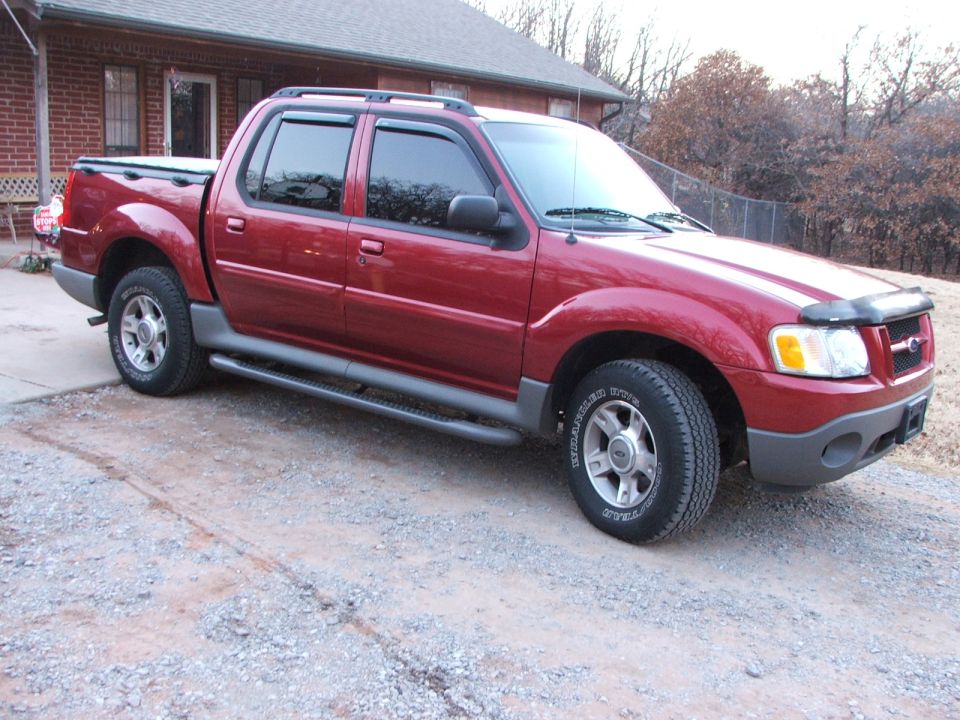 Red 2003 Ford Sport Trac pickup truck with a tonneau cover, parked on a gravel driveway