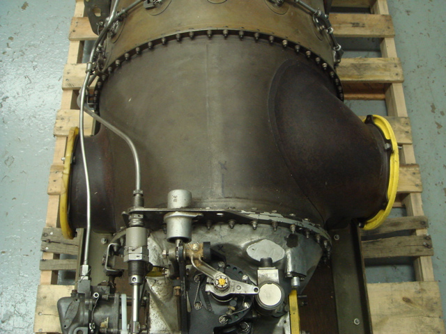 Close-up of a large metal component with yellow accents, likely a jet engine part, resting on a wooden pallet