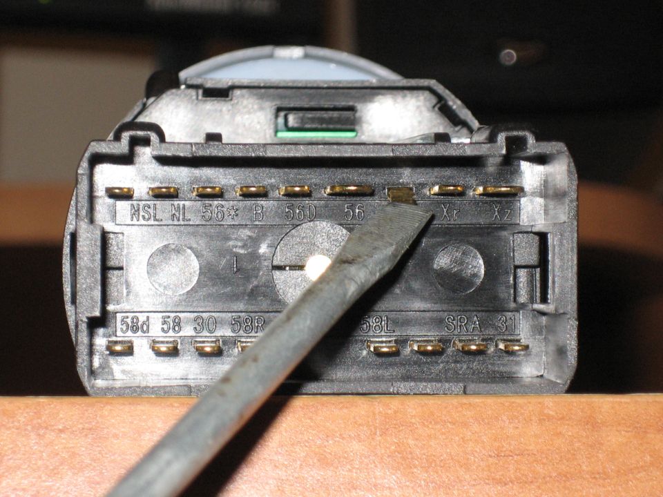 Back of a VW headlight switch showing labeled terminal pins, with a screwdriver pointing at one terminal
