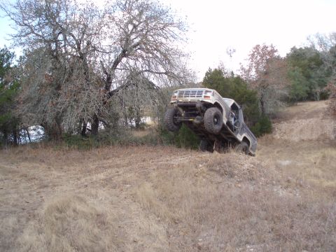 1986 Ford Bronco - A tan Ford Bronco is shown tilted on its side on a dirt hill with its front wheels off the ground.