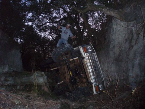 1986 Ford Bronco - This SUV has rolled over on its side, with a person standing on one of its tires.