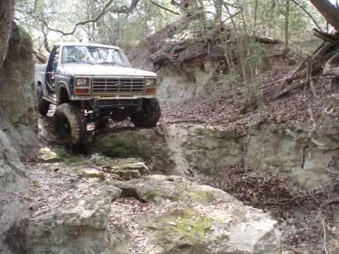 1986 Ford Bronco - This lifted truck is navigating a challenging off-road trail with steep, rocky inclines.
