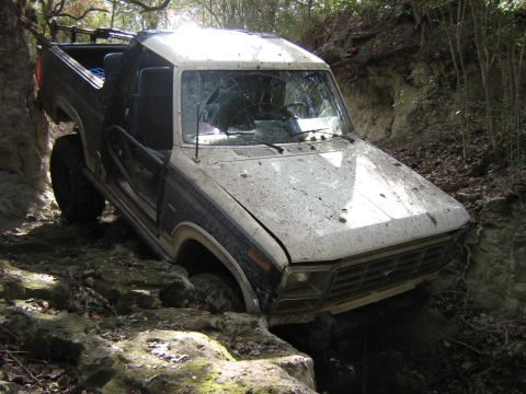 1986 Ford Bronco - This muddy Ford Bronco is stuck in a ditch, its front end angled downwards.