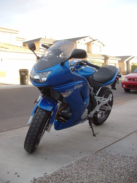 2007 Kawasaki Ninja - A blue Kawasaki Ninja motorcycle is parked on a sidewalk in front of houses. The 'Ninja' and '650R' decals are visible on the side fairing.