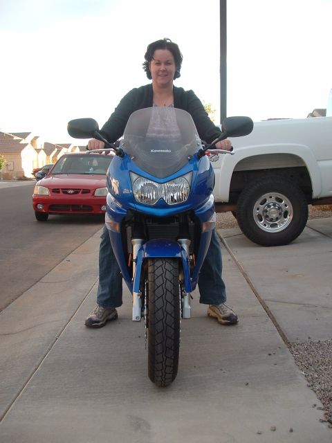 2007 Kawasaki Ninja - A blue Kawasaki motorcycle is parked on a sidewalk with a woman seated on it, and a red car and white truck in the background.