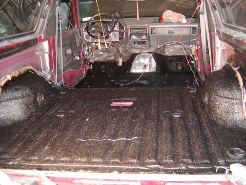 1991 Ford Bronco - The interior of a red SUV shows exposed wiring and a dark, textured floor, suggesting it is undergoing restoration.