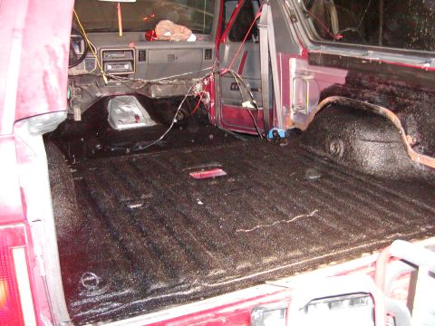 1991 Ford Bronco - The interior of a red SUV shows exposed wiring and a black spray-in bed liner covering the cargo area.