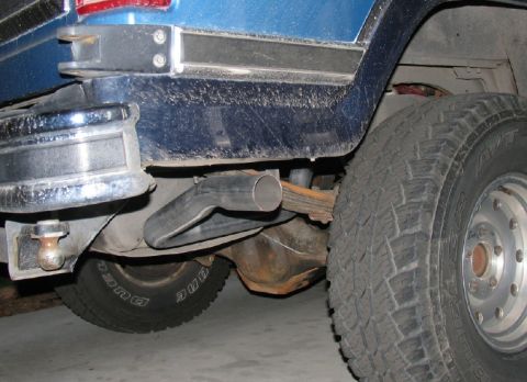 1984 Ford Bronco - Close-up view of the rear suspension and exhaust system of a blue SUV, showing the axle and a tire.