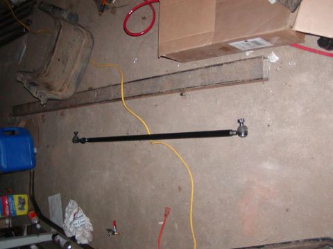 1991 Ford Bronco - Steering linkage rod with tie rod ends on a concrete floor, with various shop items in the background.