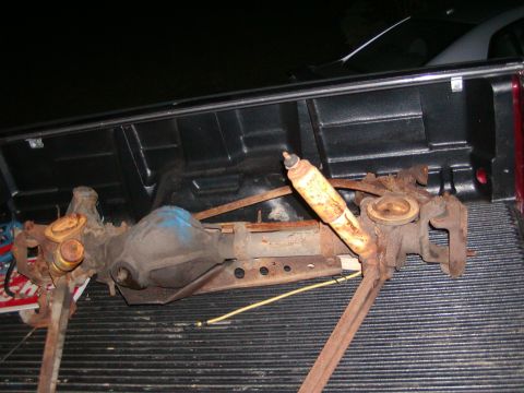 1991 Ford Bronco - A rusty rear axle assembly with a shock absorber is loaded into the bed of a pickup truck.