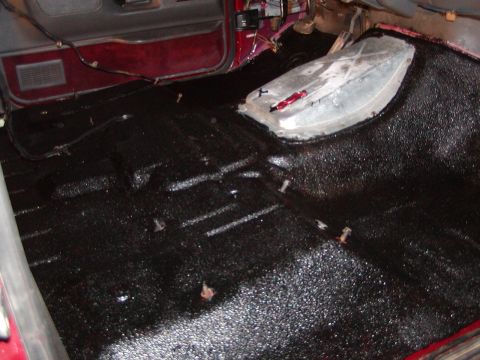 1991 Ford Bronco - The interior floor of a vehicle shows a black textured coating and a silver tunnel cover with red tape.