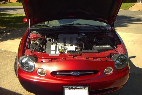 1999 Ford Taurus - The engine compartment of a red 1999 Ford Taurus is visible with the hood raised.