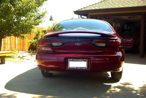 1999 Ford Taurus - Rear view of a red 1999 Ford Taurus sedan parked in a driveway, with another vehicle visible in the garage.