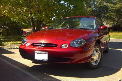 1999 Ford Taurus - This red 1999 Ford Taurus is parked outside on a sunny day. The front of the car is visible from a 3/4 angle.