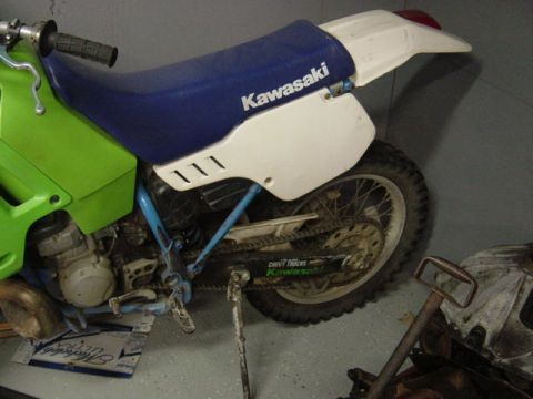 1987 Suzuki Samurai - A green and white Kawasaki dirt bike is parked indoors, showing its side profile and blue seat.