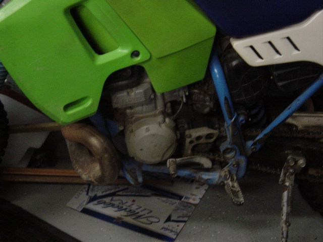 Dirt bike engine and blue frame with green plastic bodywork. Exhaust pipe visible