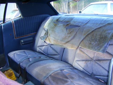 1971 Mercury Marquis - The interior of a car shows a worn rear seat with blue patterned upholstery and a torn fabric cover.