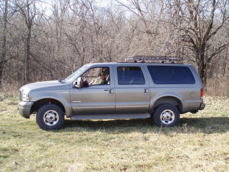 Gray Ford Excursion SUV with roof rack parked in a field