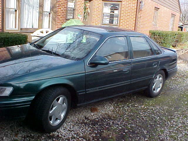 Dark green Ford Taurus sedan parked beside a brick building