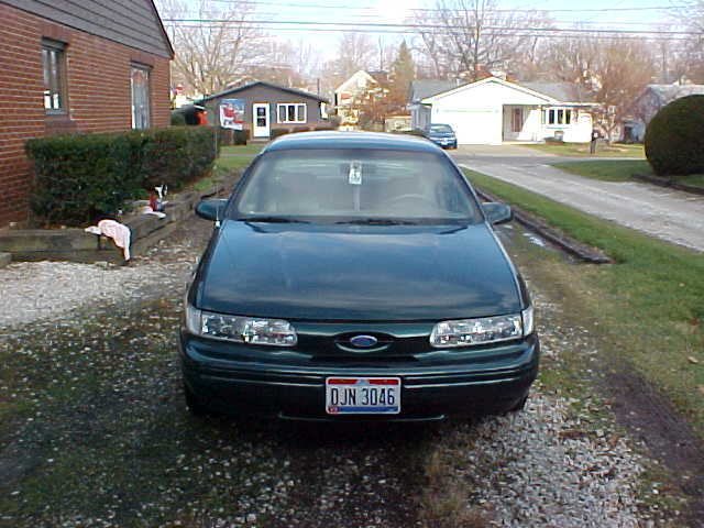 Front view of dark green Ford Taurus sedan on a gravel driveway