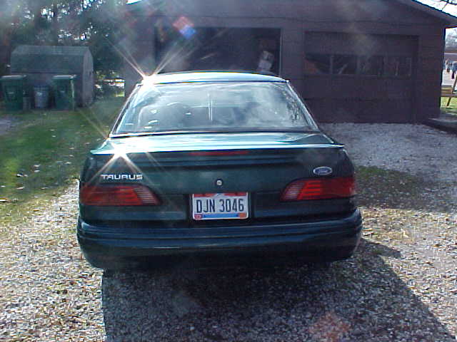 Rear view of dark green Ford Taurus sedan in front of a garage
