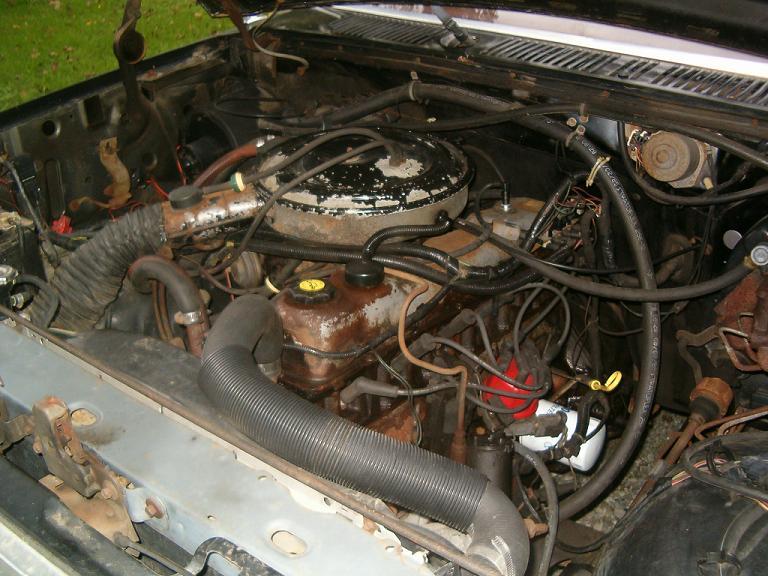 Engine bay with hoses, wires, and engine components visible. Water stains on engine parts